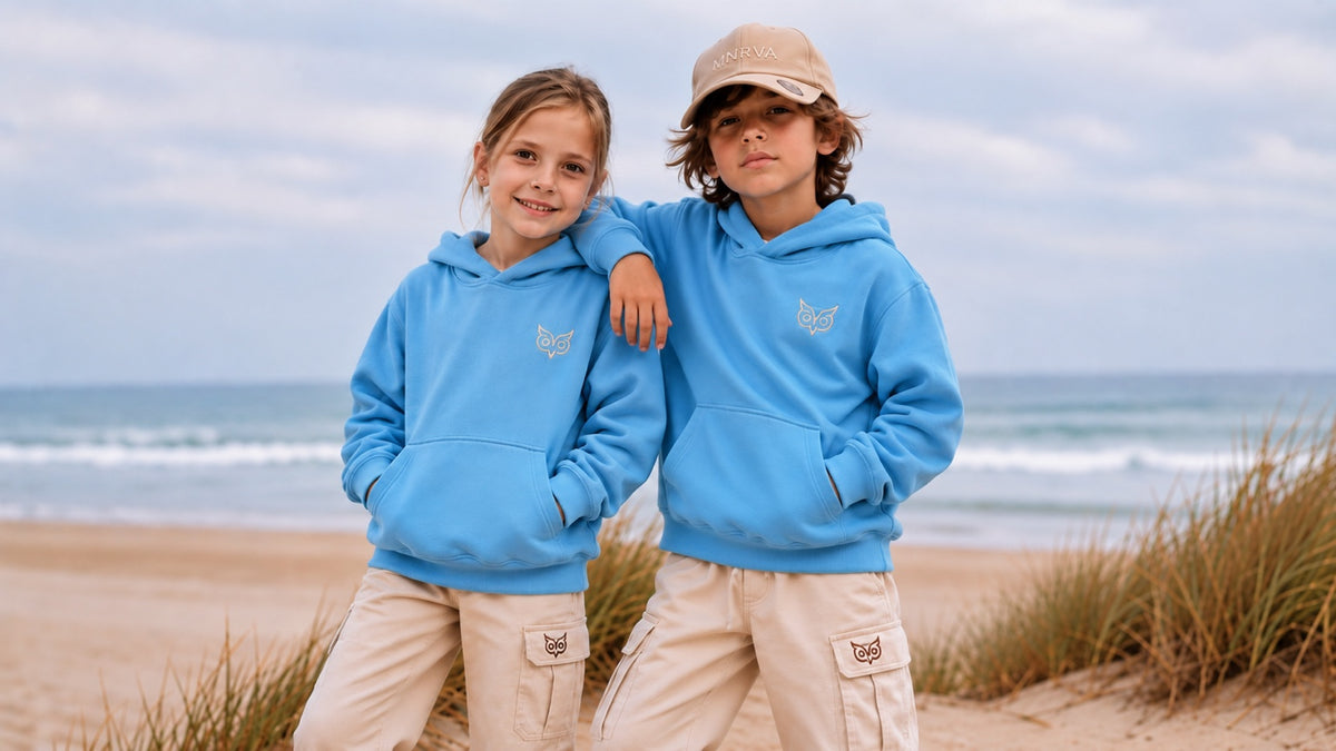 Two children wearing MNRVA Caeruleus blue hoodies and Ebur cargo pants by the coast